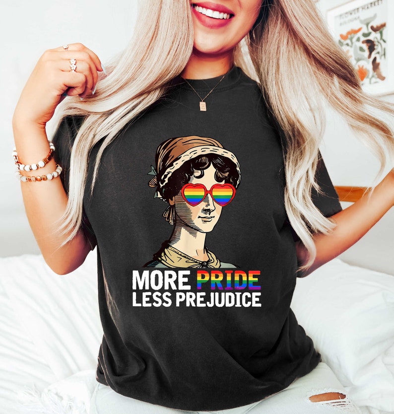 May include: Black t-shirt featuring a graphic of a woman wearing rainbow heart-shaped sunglasses and the text "More Pride Less Prejudice".