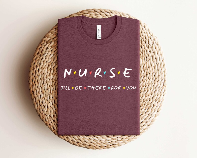 Puede incluir: Camiseta color burdeos con el texto "NURSE" en letras de colores con corazones entre cada letra. El texto "I'LL BE THERE FOR YOU" est&aacute; debajo de la palabra "NURSE" en letras negras con puntos de colores entre cada palabra.