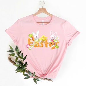 May include: Pink t-shirt with a graphic of two bunnies and a chick holding the word "Easter" in orange letters.