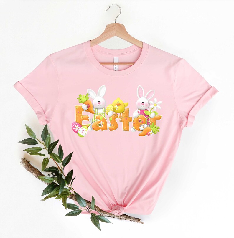 May include: Pink t-shirt with a graphic of two bunnies and a chick holding the word "Easter" in orange letters.