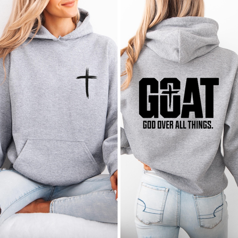 Pode incluir: Um moletom cinza claro com um bolso frontal e capuz com cord&atilde;o. A frente apresenta uma cruz preta, e as costas exibem a palavra "GOAT" com uma cruz no "O", e o texto "GOD OVER ALL THINGS."