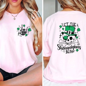 May include: Pink t-shirt with a skeleton hand giving the middle finger with shamrocks and stars on the front and a skull wearing a green leprechaun hat with the text "Let the Shenanigans Begin" on the back.