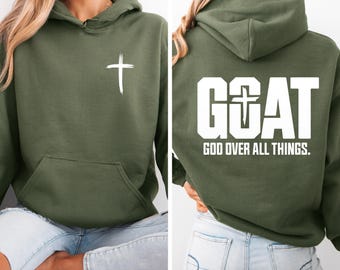 May include: An olive green hoodie with a white cross on the front and the text "GOAT GOD OVER ALL THINGS" on the back. It has a hood and a front pocket. Made of a soft material.