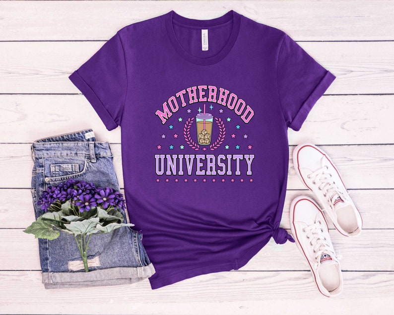 May include: Purple t-shirt with the text "Motherhood University" in pink and white letters. A cartoon image of a boba tea drink is in the center of the text.