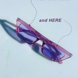 May include: A pair of purple cat-eye sunglasses with a light blue lens. The sunglasses are lying on a white surface.