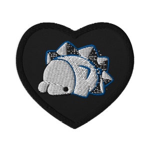 Puede incluir: Parche bordado en forma de corazón negro. El parche presenta un dinosaurio blanco con detalles azules y un patrón de cuadros en la espalda. El dinosaurio está tumbado. El parche es adecuado para ropa o accesorios.