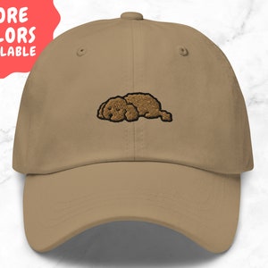 Peut inclure: Une casquette de baseball beige avec un chien brun brodé endormi dessus.