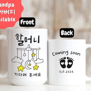 May include: White ceramic mug with a black design. The front of the mug says "할머니 기다려 주세요" which translates to "Grandma, please wait" and features a mobile with stars, clouds, and a crescent moon. The back of the mug says "Coming soon est. 2024" and features two black footprints with hearts.