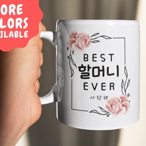 May include: White ceramic mug with a black outline of a floral design and the text "BEST 엄마니 EVER" in black and Korean. The text "사랑 듬뿍" is in smaller font below the main text.