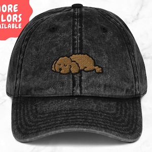 May include: A black distressed denim baseball cap with an embroidered brown sleeping dog design.