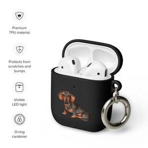 Op de afbeelding: Zwarte siliconen hoes voor Apple AirPods met een teckelprint en een zilveren karabijnhaak.