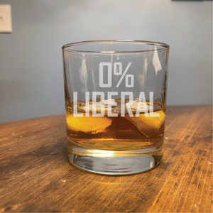 May include: A clear glass tumbler with the text "0% LIBERAL" etched on the side. The glass is filled with amber liquid and ice cubes.
