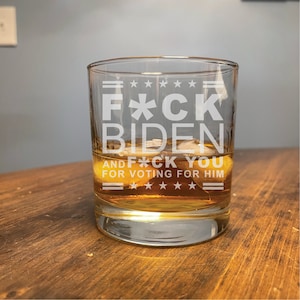 May include: A clear glass tumbler with the text "F*CK BIDEN AND F*CK YOU FOR VOTING FOR HIM" etched on the side. The glass is filled with a brown liquid and ice cubes.