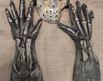 May include: A white hockey mask with a black strap and two skeletal hand props. The mask has a hole in the left eye area and is covered in brown and black paint.