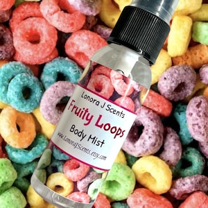 May include: A clear glass bottle with a black spray top and a white label that reads "Lonora J Scents Fruity Loops Body Mist www.LonoraJScents.etsy.com". The bottle is sitting on a bed of colorful cereal loops.
