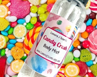 May include: A clear glass bottle with a black spray top and a white label. The label has a pink background with a watercolor design of candy and lollipops. The text on the label reads "Lonora J Scents Candy Crush Body Mist www.LonoraJScents.etsy.com". The bottle is surrounded by colorful candy and lollipops.