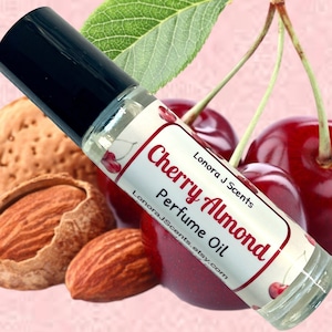 May include: A clear glass roll-on bottle with a black cap and a white label that reads "Cherry Almond Perfume Oil" and "Lonora J Scents.etsy.com". The bottle is sitting on top of almonds and cherries.
