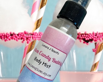 May include: A clear glass bottle with a black spray top and a pink, blue, and white label that reads "Lonora J Scents Cotton Candy Bubbly Body Mist www.LonoraJScents.etsy.com".