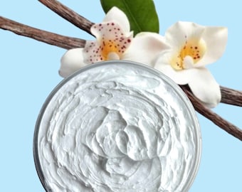 Op de afbeelding: Een witte, romige body butter in een glazen pot met een swirl-patroon. De pot is omringd door vanillebonen en witte orchideeën.
