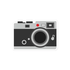 May include: A vintage-style silver camera with a black lens and a red button on top. The camera has a silver dial on the right side.