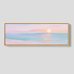 May include: A panoramic landscape painting in a light wood frame depicting a serene beach scene at sunrise. The artwork features soft pastel hues of pink, peach, and light blue, with a pale sun reflecting on the calm water and sandy shore.