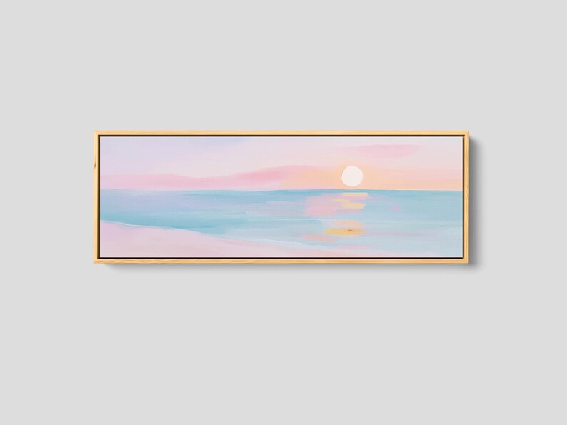 May include: A panoramic landscape painting in a light wood frame depicting a serene beach scene at sunrise. The artwork features soft pastel hues of pink, peach, and light blue, with a pale sun reflecting on the calm water and sandy shore.