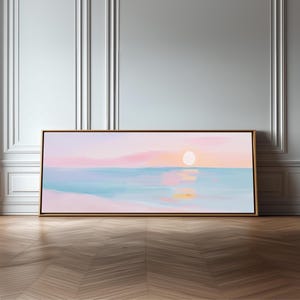 May include: A rectangular landscape painting in a thin wooden frame featuring a soft-toned sunset over a calm ocean. The artwork displays pastel pink and orange clouds above a light blue sea, with a pale sun reflecting on the water surface.