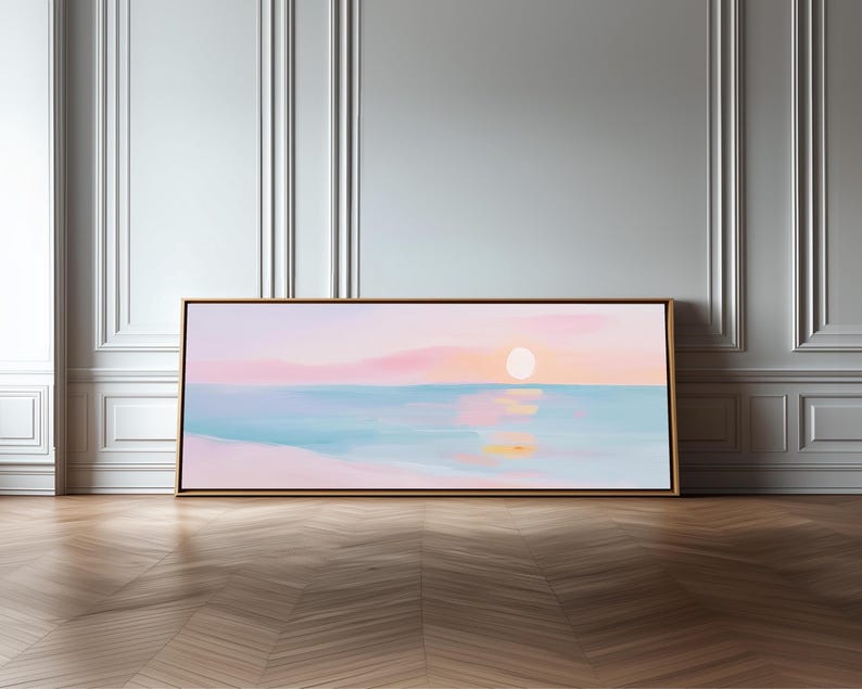 May include: A rectangular landscape painting in a thin wooden frame featuring a soft-toned sunset over a calm ocean. The artwork displays pastel pink and orange clouds above a light blue sea, with a pale sun reflecting on the water surface.