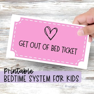Puede incluir: Un boleto rectangular rosa con un borde blanco discontinuo, un icono de corazón dibujado a mano en negro y el texto negro "GET OUT OF BED TICKET" impreso en el centro. Debajo del boleto, el texto "Printable BEDTIME SYSTEM FOR KIDS" es visible.