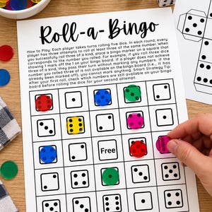 May include: A Roll-a-Bingo game sheet with instructions and a grid of dice faces. The sheet features colorful translucent plastic markers placed on specific squares. Two white six-sided dice are positioned near the top of the paper.