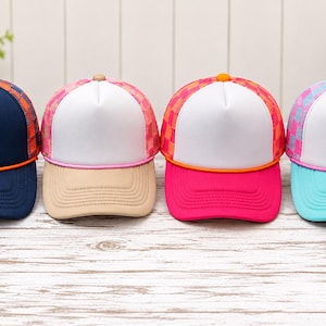 May include: Four trucker hats with white front panels and mesh backs. The first is navy with orange accents, the second is beige with pink accents, the third is bright pink with orange accents, and the fourth is light blue with pink accents.