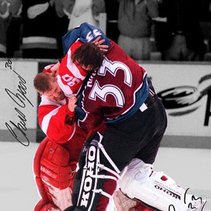 May include: Two hockey players in a game, one in a red and white jersey with the number 30, the other in a blue and red jersey with the number 33. The player in the red and white jersey is being held down by the player in the blue and red jersey. The player in the red and white jersey has a signature that says "Gino Odjick" on the ice. The player in the blue and red jersey has a signature that says "H.23" on the ice.