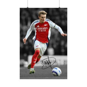 May include: A poster featuring a soccer player in a red and white Arsenal jersey with Emirates Fly Better text, white shorts, and red socks, dribbling a soccer ball. The image is in color while the background is black and white with a black signature.
