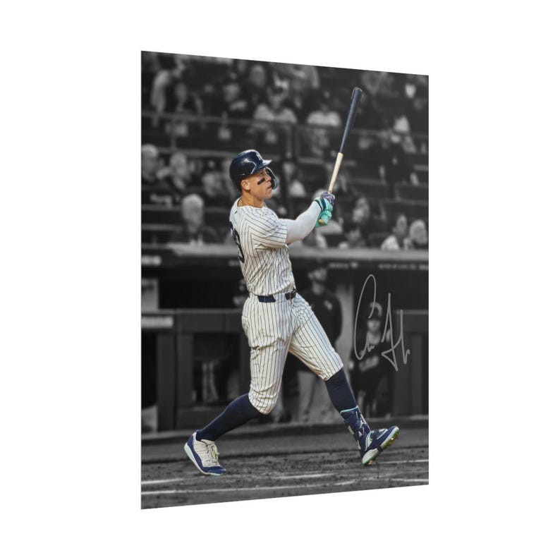 May include: A black and white photograph of a baseball player in a pinstriped uniform swinging a bat. The player wears a helmet and dark socks. A prominent signature is visible on the right side of the image against the blurred stadium background.