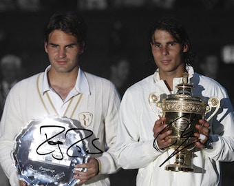 May include: Two men in white tennis uniforms holding trophies. The man on the left is holding a silver tray with a signature on it. The man on the right is holding a gold trophy with a handle.