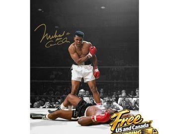 Puede incluir: Una fotografía en blanco y negro de Muhammad Ali de pie sobre un oponente caído en un ring de boxeo. Ali viste pantalones cortos blancos y guantes de boxeo rojos. Una firma dorada es visible en la esquina superior izquierda de la imagen.