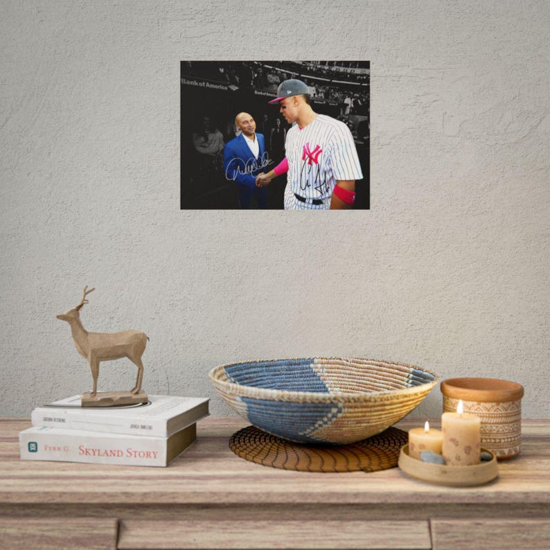 Puede incluir: Una fotograf&iacute;a enmarcada que muestra a un jugador de b&eacute;isbol con una camiseta blanca a rayas con un logotipo rojo y a una persona con un traje azul d&aacute;ndose la mano. La imagen incluye dos firmas distintas en tinta negra sobre la superficie.