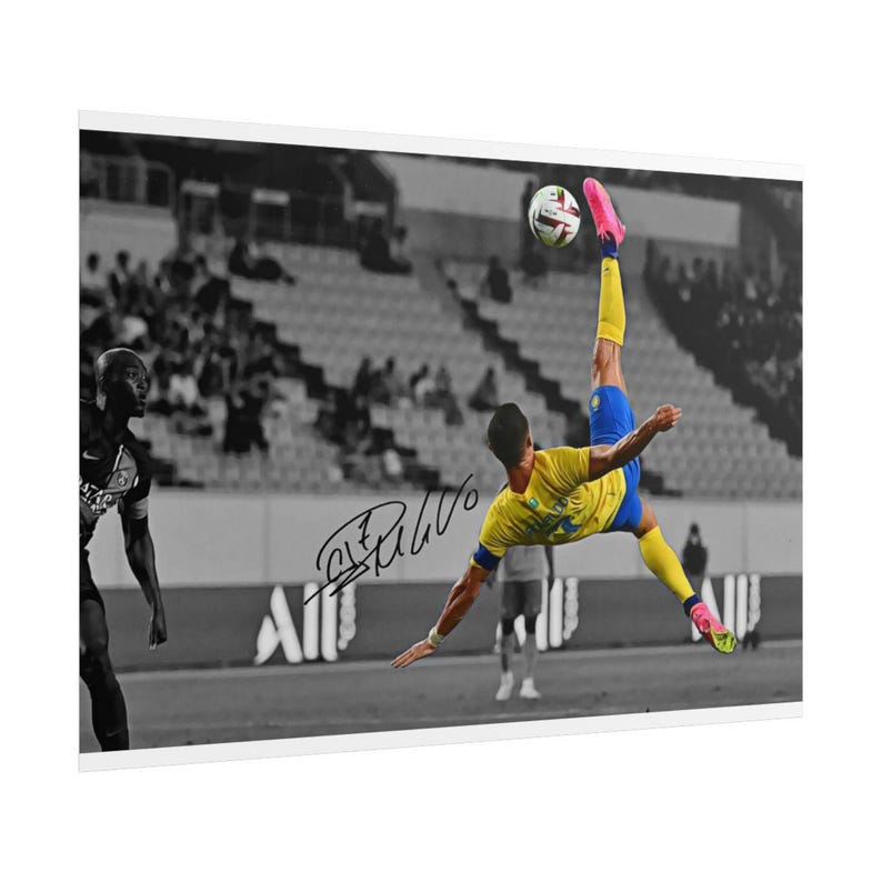 May include: A black and white photograph featuring a soccer player in a yellow jersey and blue shorts performing a bicycle kick to strike a soccer ball. The player wears bright pink cleats. A signature is visible on the print over the stadium background.