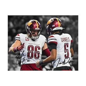 May include: A photograph of two football players wearing white Washington Commanders jerseys with burgundy and gold accents. One player wears number 86 and the other wears number 5 with the name DANIELS on the back. Both jerseys feature autographs.