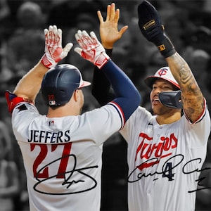 Può includere: Due giocatori di baseball in uniforme bianco con accenti rossi e blu si danno il cinque. Il giocatore a sinistra indossa un casco nero con il numero 27 e il nome "JEFFERS" sul retro della sua maglia. Il giocatore a destra indossa un casco nero con il numero 4 e il nome "CARRILLO" sul retro della sua maglia. Entrambi i giocatori indossano guanti bianchi.