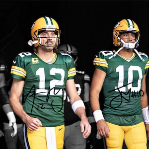 May include: Two Green Bay Packers football players wearing green and yellow jerseys with their numbers, 12 and 10, on the front. The player on the left is wearing a helmet with a green and yellow design and the player on the right is wearing a helmet with a green and yellow design. The players are standing in a dark room.