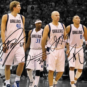 May include: Four basketball players wearing white jerseys with the word "Dallas" and their jersey numbers. The players are standing on a basketball court with a crowd of spectators in the background.