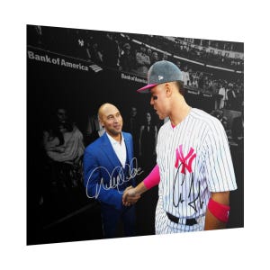 Puede incluir: Una fotograf&iacute;a en blanco y negro que muestra a un hombre con traje azul estrechando la mano de un jugador de b&eacute;isbol con camiseta a rayas, logotipo rosa y mu&ntilde;equeras rosas. La imagen incluye dos firmas y un letrero de Bank of America.
