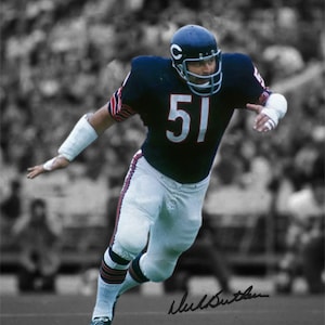 Puede incluir: Una fotografía en blanco y negro de un jugador de fútbol americano que lleva una camiseta azul con el número 51. El jugador corre con el balón y tiene una mirada decidida. La foto está firmada por el jugador, "Dick Butkus".