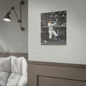 May include: A square wall poster featuring a black and white action photograph of a baseball player in a pinstriped uniform swinging a bat. The player wears a helmet and athletic gear. A handwritten signature is visible on the right side.