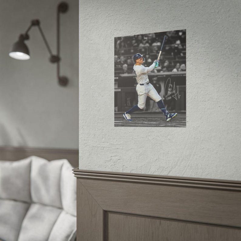 May include: A square wall poster featuring a black and white action photograph of a baseball player in a pinstriped uniform swinging a bat. The player wears a helmet and athletic gear. A handwritten signature is visible on the right side.