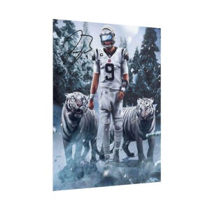 Pode incluir: Um cartaz vertical apresentando um jogador de futebol americano com uniforme branco e o n&uacute;mero 9, em p&eacute; entre dois tigres brancos numa floresta nevada. O jogador usa um capacete e uma assinatura a tinta preta est&aacute; no canto superior esquerdo.