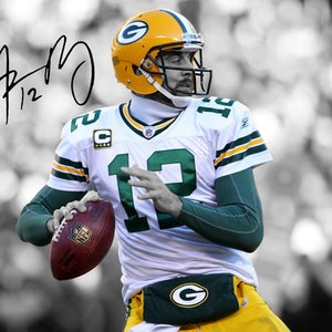 May include: A football player wearing a green and white jersey with the number 19 on it. He is holding a football and wearing a green helmet with a white stripe. The player's signature is visible in the top left corner of the image.