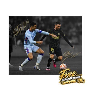 May include: A photograph of two soccer players in action on a field. One player wears a light blue jersey and white shorts, while the other wears a black jersey and black shorts with the number 30. Both players have gold signatures on the image.