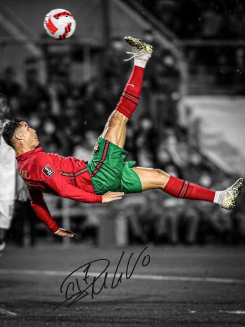 May include: A footballer in a red long-sleeved shirt and green shorts performs an overhead kick to strike a white, red and black football in mid-air. The player wears red socks and gold boots. A black signature is visible at the bottom of the image.
